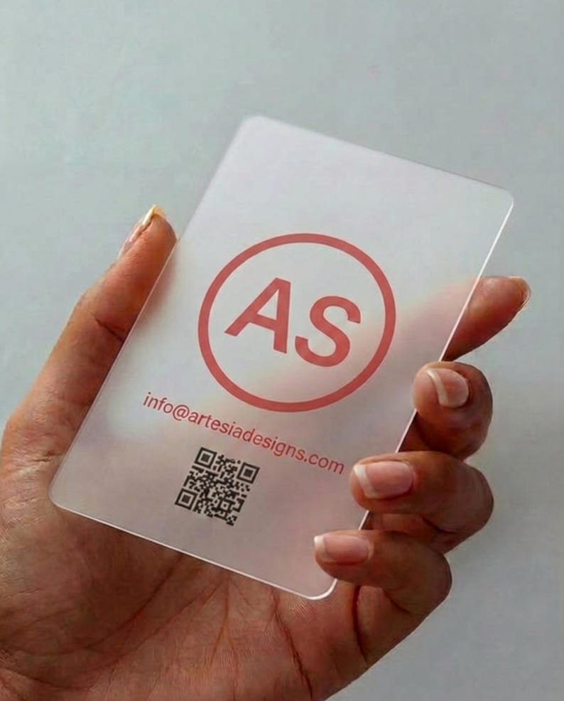May include: A rectangular, semi-transparent frosted business card featuring a coral-colored circular logo with the letters AS inside. Below the logo, the text info@artesiadesigns.com is printed in coral, followed by a black square QR code.