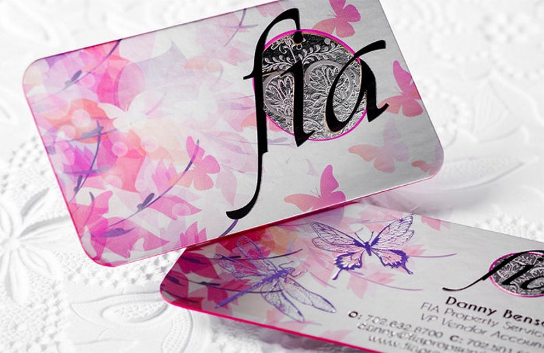 May include: Two business cards with a pink and purple floral design. The top card has the word "fla" in black script with a silver circle behind it. The bottom card has the text "Danny Bense" and "FIA Property Services" in black text.