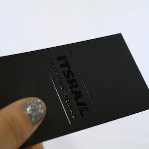 May include: A rectangular black business card featuring the text ITSRAIL INTERNATIONAL in a glossy raised ink finish. The card has a matte black surface with the company name printed in a bold, dark font, creating a subtle contrast between the textures.
