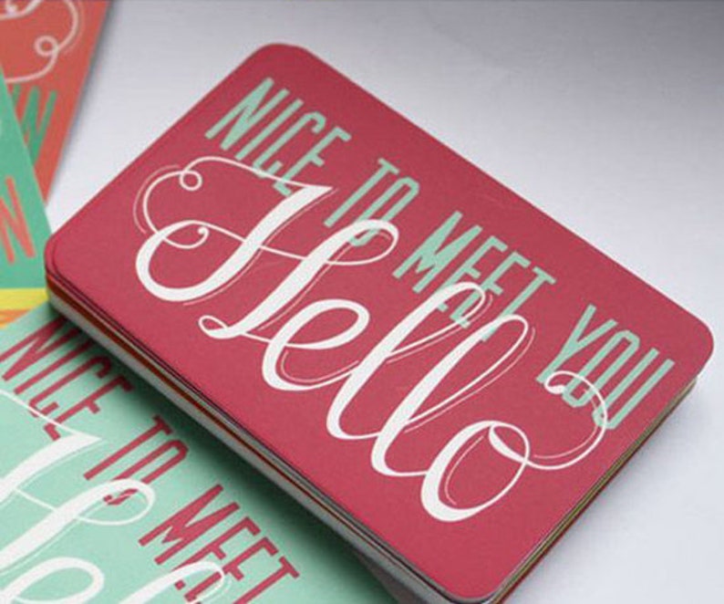 May include: A stack of rectangular business cards with rounded corners. The top card is red with the word Hello in large white script and the text NICE TO MEET YOU in light green block letters. Other cards in the stack feature inverted colors.
