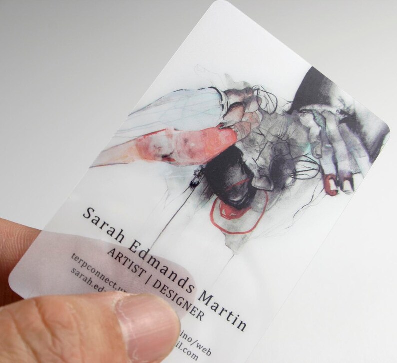 May include: A translucent rectangular business card featuring a detailed watercolor illustration of hands in shades of black, white, and red. The text reads Sarah Edmans Martin, ARTIST | DESIGNER, along with contact information in black sans-serif font.