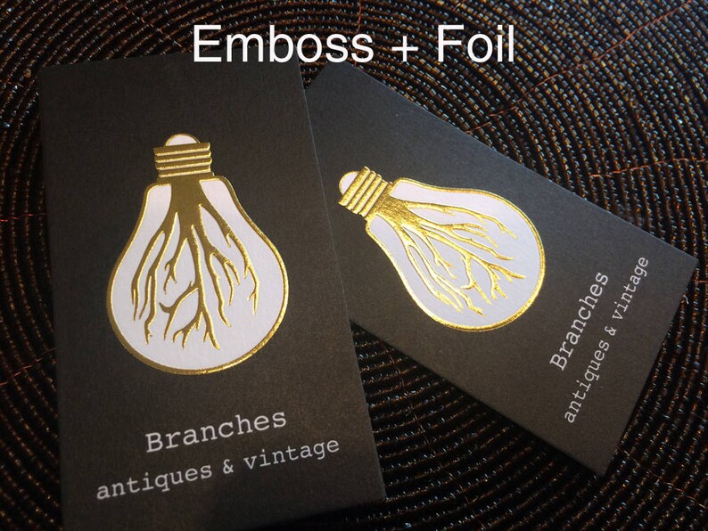 May include: Two black business cards with a gold foil design of a lightbulb with tree-like roots. The cards have the text "Branches antiques & vintage" in white. The words "Emboss + Foil" are at the top.