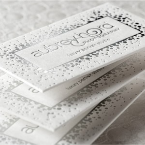 May include: A stack of white rectangular business cards featuring silver foil accents in a scattered dot pattern. The top card displays the text aubrey hord photography luxury portrait studio in a clean, sans-serif font with embossed lettering.