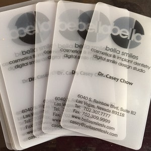 May include: A stack of four translucent, frosted plastic business cards for Bella Smiles. The cards feature black text including the name Dr. Casey Chow, the address 6040 S. Rainbow Blvd, Suite B2, Las Vegas, Nevada 89118, and contact details.