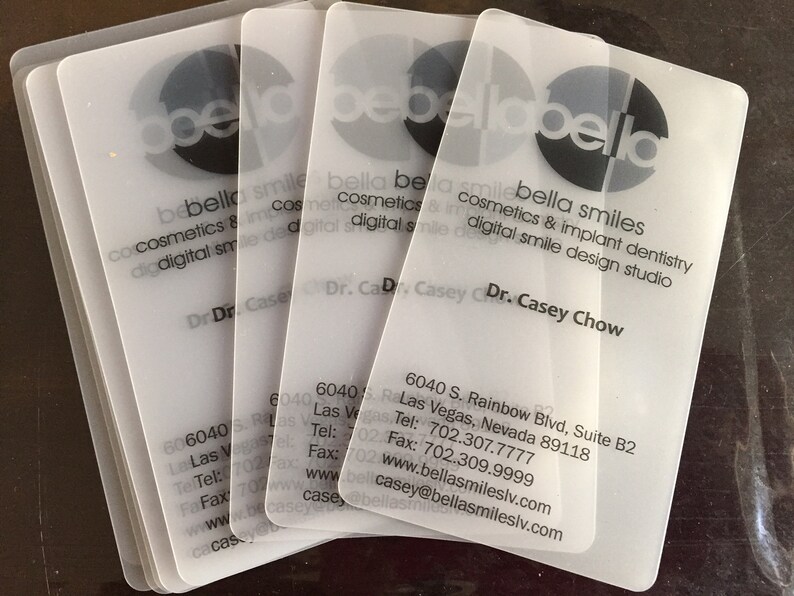 May include: A stack of four translucent, frosted plastic business cards for Bella Smiles. The cards feature black text including the name Dr. Casey Chow, the address 6040 S. Rainbow Blvd, Suite B2, Las Vegas, Nevada 89118, and contact details.