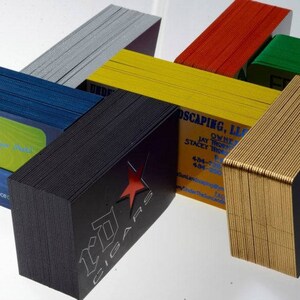 May include: Stacks of business cards in various colors, including black, gold, red, green, blue, and yellow. The cards are stacked in a creative, geometric pattern. Some of the cards have text on them, including "OMN" and "Princecraft".