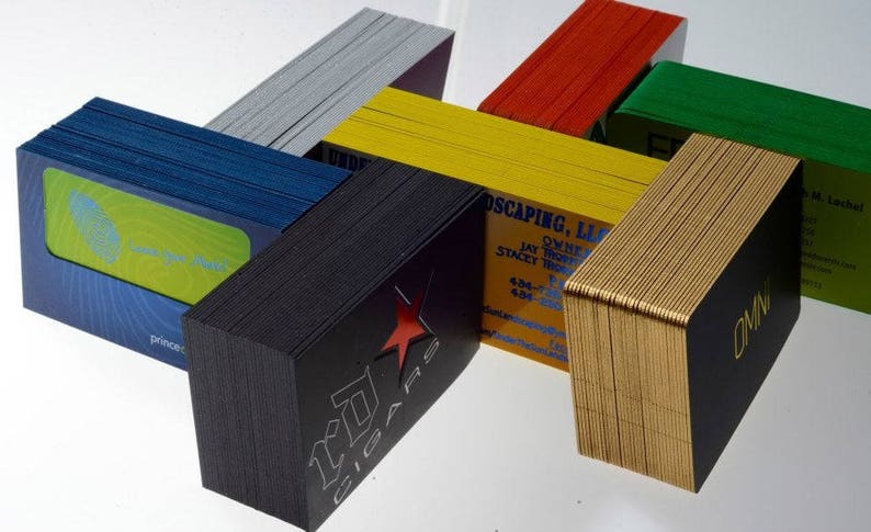May include: Stacks of business cards in various colors, including black, gold, red, green, blue, and yellow. The cards are stacked in a creative, geometric pattern. Some of the cards have text on them, including "OMN" and "Princecraft".