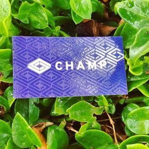 May include: A rectangular business card with a deep purple background featuring a repeating geometric pattern of white interlocking squares. The word CHAMP is printed in white capital letters next to a white diamond-shaped logo icon.