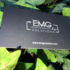 May include: Black business card with white text and a logo. The logo is a stylized image of a cable with the letters "EMG" and the words "SOLUTIONS" below. The website address "www.emgsolutions.biz" is printed at the bottom of the card.