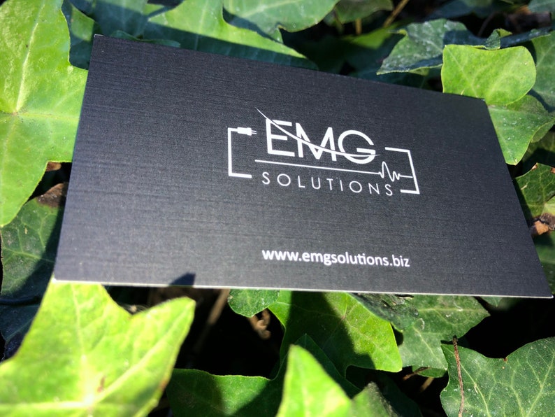 May include: Black business card with white text and a logo. The logo is a stylized image of a cable with the letters "EMG" and the words "SOLUTIONS" below. The website address "www.emgsolutions.biz" is printed at the bottom of the card.