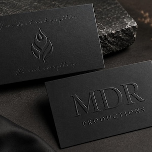 May include: Two rectangular black business cards with embossed details. One card features a flame-like logo and the text "If we don't risk anything, We risk everything." The other card displays the text "MDR PRODUCTIONS" in a serif font.
