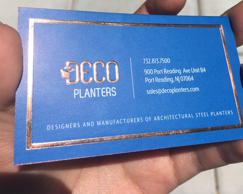 May include: A business card with a blue background and copper-colored text and border. The card features the logo "DECO PLANTERS" and contact information. The text "DESIGNERS AND MANUFACTURERS OF ARCHITECTURAL STEEL PLANTERS" is also visible.