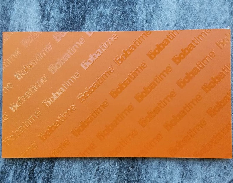 May include: A rectangular orange sheet featuring a repeating pattern of the word bobatime embossed across the surface in diagonal lines. The text is oriented in a consistent direction, creating a textured appearance on the flat orange material.