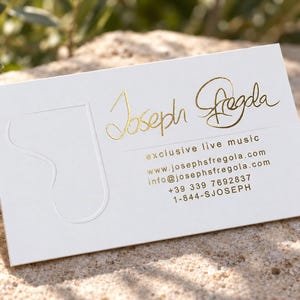 Puede incluir: Una tarjeta de visita rectangular blanca con el nombre Joseph Fregola en relieve de l&aacute;mina dorada, el texto exclusive live music, un sitio web, correo electr&oacute;nico y n&uacute;meros de tel&eacute;fono. Un gran logotipo de la letra J est&aacute; grabado a la izquierda.