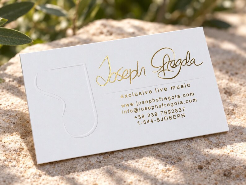 Puede incluir: Una tarjeta de visita rectangular blanca con el nombre Joseph Fregola en relieve de l&aacute;mina dorada, el texto exclusive live music, un sitio web, correo electr&oacute;nico y n&uacute;meros de tel&eacute;fono. Un gran logotipo de la letra J est&aacute; grabado a la izquierda.