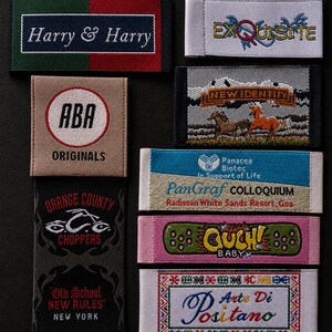 May include: A collection of eight rectangular woven fabric labels featuring various embroidered designs and text including Harry & Harry, Exquisite, ABA Originals, New Identity with horses, Panacea Biotec, Orange County Choppers, Ouch Baby, and Arte Di Positano.