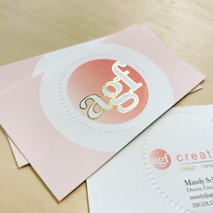 Puede incluir: Tarjetas de visita rectangulares con fondo rosa p&aacute;lido y un c&iacute;rculo blanco central con borde punteado. El texto en l&aacute;mina dorada dice agf creatives. Una segunda tarjeta muestra el logotipo agf, el texto creatives, design consultant y datos de contacto.