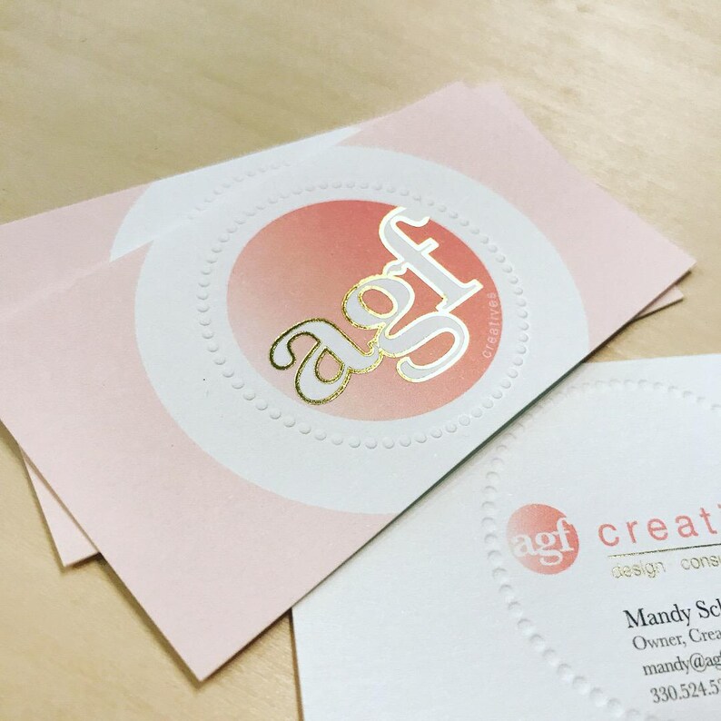 Puede incluir: Tarjetas de visita rectangulares con fondo rosa p&aacute;lido y un c&iacute;rculo blanco central con borde punteado. El texto en l&aacute;mina dorada dice agf creatives. Una segunda tarjeta muestra el logotipo agf, el texto creatives, design consultant y datos de contacto.