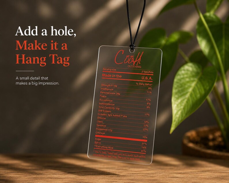 Puede incluir: Una etiqueta colgante rectangular de acr&iacute;lico transparente suspendida por un cord&oacute;n negro. La etiqueta presenta texto impreso en rojo que se asemeja a una etiqueta de informaci&oacute;n nutricional con la marca Coah Clothing y varios atributos.
