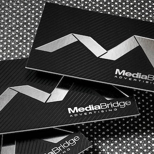 May include: Close-up of black business cards with a silver embossed logo and the text "MediaBridge Advertising".