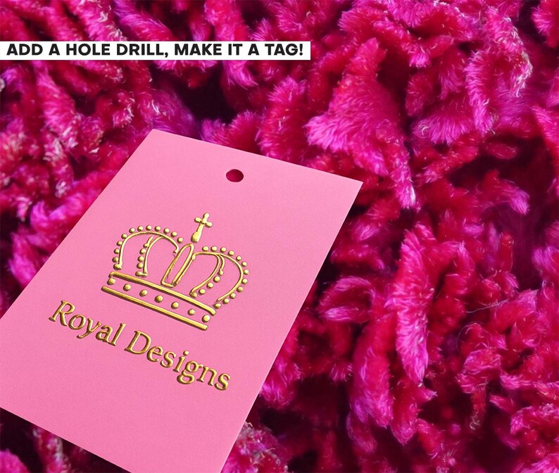 Puede incluir: Una etiqueta rectangular rosa con un icono de corona dorada y el texto Royal Designs en letras doradas. La etiqueta tiene un agujero preperforado en la parte superior central. El texto ADD A HOLE DRILL, MAKE IT A TAG! es visible arriba a la izquierda.
