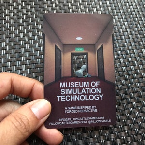 Puede incluir: Una tarjeta de juego rectangular con una ilustraci&oacute;n de un pasillo con una pieza de ajedrez blanca, el texto MUSEUM OF SIMULATION TECHNOLOGY, A GAME INSPIRED BY FORCED PERSPECTIVE, e informaci&oacute;n de contacto como INFO@PILLOWCASTLEGAMES.COM y PILLOWCASTLEGAMES.COM.