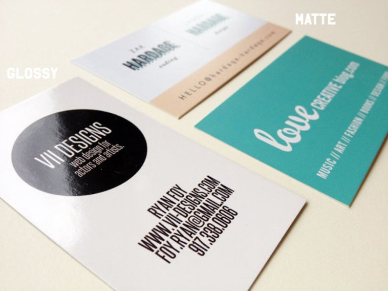 Puede incluir: Tres tarjetas de visita rectangulares con acabados variados. Una tarjeta blanca brillante presenta un c&iacute;rculo negro con el texto VII DESIGNS, web design for actors and artists, y datos de contacto. Una tarjeta mate de color verde azulado dice love creative blog.com.