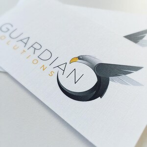 May include: A white business card with the text "GUARDIAN SOLUTIONS" in black and a stylized black and gray eagle with a yellow beak flying in a circle.