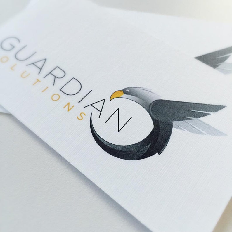 May include: A white business card with the text "GUARDIAN SOLUTIONS" in black and a stylized black and gray eagle with a yellow beak flying in a circle.