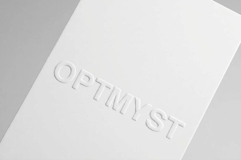 May include: A rectangular white card featuring the word OPTMYST embossed in capital letters across the center. The lettering is raised, creating a subtle three-dimensional effect against the smooth, matte white surface of the card stock.