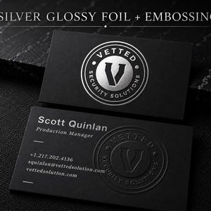 May include: Two black business cards featuring the text SILVER GLOSSY FOIL + EMBOSSING. One card displays a circular silver foil logo for Vetted Security Solutions. The other card shows the name Scott Quinlan, contact details, and a blind embossed logo.