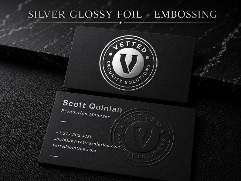 May include: Two black business cards featuring the text SILVER GLOSSY FOIL + EMBOSSING. One card displays a circular silver foil logo for Vetted Security Solutions. The other card shows the name Scott Quinlan, contact details, and a blind embossed logo.