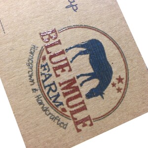 May include: A close-up of a brown paper label with the words "Blue Mule Farm" in red and a blue mule silhouette inside a circular design. The label also includes the text "Handcrafted" and "Honegrown". The word "Soap" is written in black.