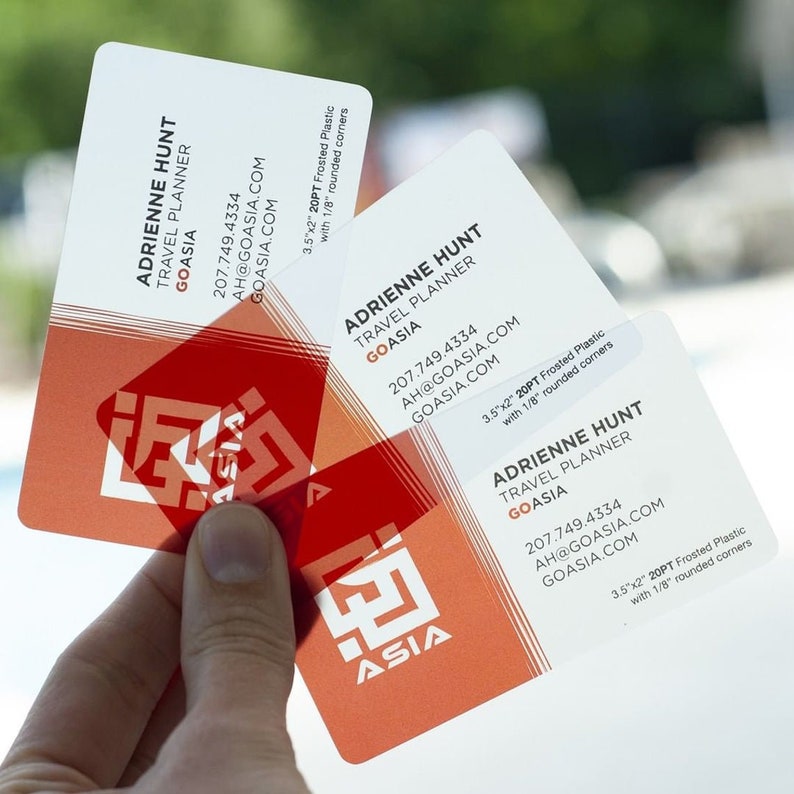 May include: Three rectangular frosted plastic business cards with rounded corners, measuring 3.5 inches by 2 inches. The cards feature the name Adrienne Hunt, Travel Planner, GoAsia, contact details, and a red geometric logo on a white background.