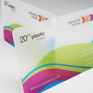 May include: Two rectangular 20PT frosted plastic business cards featuring a personal trainer logo with three colored arrows. The design includes wavy bands of lime green, magenta, and cyan, with printed contact information and a website address.