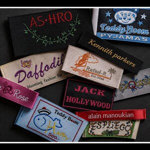 May include: A collection of rectangular fabric clothing labels featuring various embroidered designs and text including AS-HRO, Teddy Boom Pyjamas, Kennith parkers, Daffodil, Rafael-R, Lila Rose, JACK HOLLYWOOD, EXQUISITE, Teddy Boom Happy sea, alain manoukian, and ESPLIEGO.