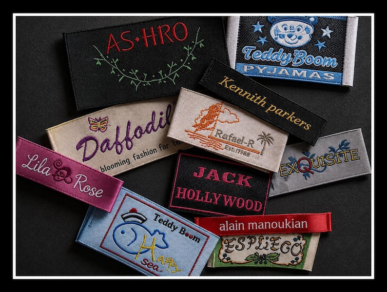 May include: A collection of rectangular fabric clothing labels featuring various embroidered designs and text including AS-HRO, Teddy Boom Pyjamas, Kennith parkers, Daffodil, Rafael-R, Lila Rose, JACK HOLLYWOOD, EXQUISITE, Teddy Boom Happy sea, alain manoukian, and ESPLIEGO.