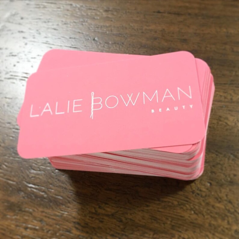 K&ouml;nnte beinhalten: Ein Stapel rosa Visitenkarten mit dem Text "Lalie Bowman Beauty" in wei&szlig;er Schrift.