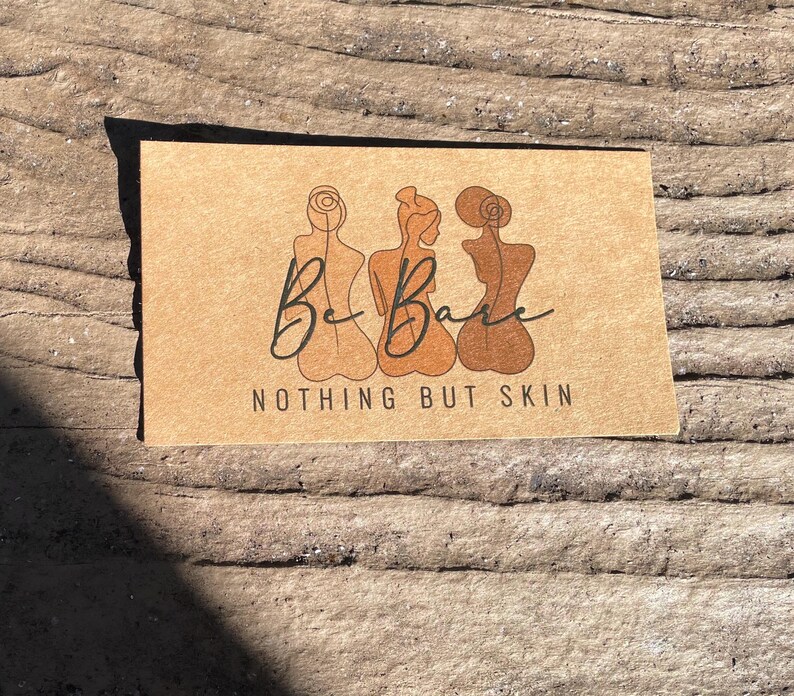 May include: A rectangular tan card featuring a black line art illustration of three figures from the back. The text "Be Bare" is written in a cursive script above the words "NOTHING BUT SKIN" printed in a clean, sans-serif black font.