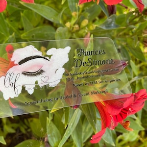 May include: A clear plastic business card with black text. The text reads "lbf Frances DeSimone looksbyfrankie@gmail.com @looksbyfrankie Email or DM for inquiries Specializing in Bridal & Event Makeup!"