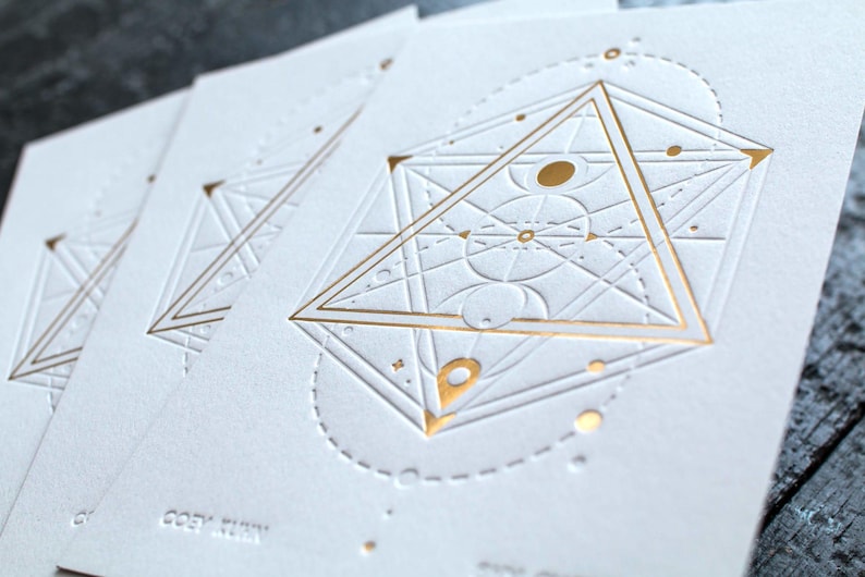 May include: A set of white rectangular cards featuring an embossed geometric design with gold foil accents. The central motif consists of a large triangle, intersecting lines, and circular elements. The text COEY KUNN is embossed at the bottom.