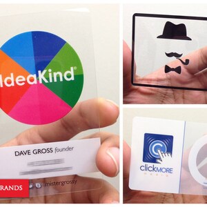 Puede incluir: Tres tarjetas de visita rectangulares de pl&aacute;stico transparente. Una presenta un logotipo circular colorido con el texto IdeaKind y Dave Gross founder. Otra muestra una silueta negra de sombrero, bigote y pipa con el texto Thea Green I Tell Stories. La tercera muestra un logotipo azul con el texto clickMore Media y Tom Ham.