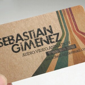May include: A rectangular business card made of light brown textured paper. The card features the black text SEBASTIAN GIMENEZ, AUDIO.VIDEO.ANIMATION, and sebiche23@hotmail.com. Diagonal stripes in green, tan, and red extend across the right side.