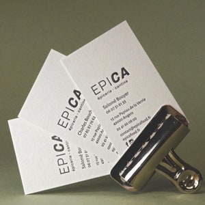 以下が含まれることがあります： EPICA &eacute;picerie - cantineという黒い文字と連絡先、住所が記載された3枚の白い長方形の名刺。名刺は右下の光沢のある銀色の金属製バインダークリップでまとめられています。