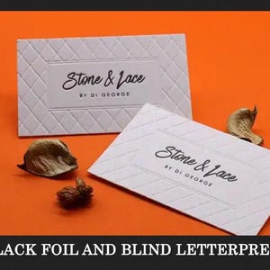 May include: Two rectangular white business cards featuring a blind letterpress diamond pattern and the black text Stone & Lace BY DI GEORGE. The cards are displayed against a solid orange background with small dried botanical elements nearby.
