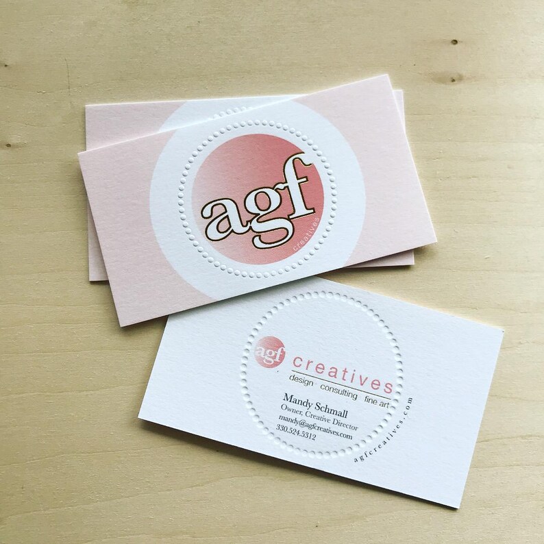 Puede incluir: Dos tarjetas de visita rectangulares. La tarjeta superior es de color rosa claro con un c&iacute;rculo blanco que contiene las letras agf en degradado rosa. La tarjeta inferior es blanca con un c&iacute;rculo rosa, el texto agf creatives y datos de contacto.