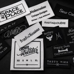 May include: A collection of rectangular fabric clothing labels in black and white. The labels feature various brand names, logos, and text including Space and Place, Makersnine, Sew Cozy, Rayan, trash to treasure, Territory Built Co, Hinara, MaddyMoo, dom streater, Doggie Duds, and Tasty Ties.