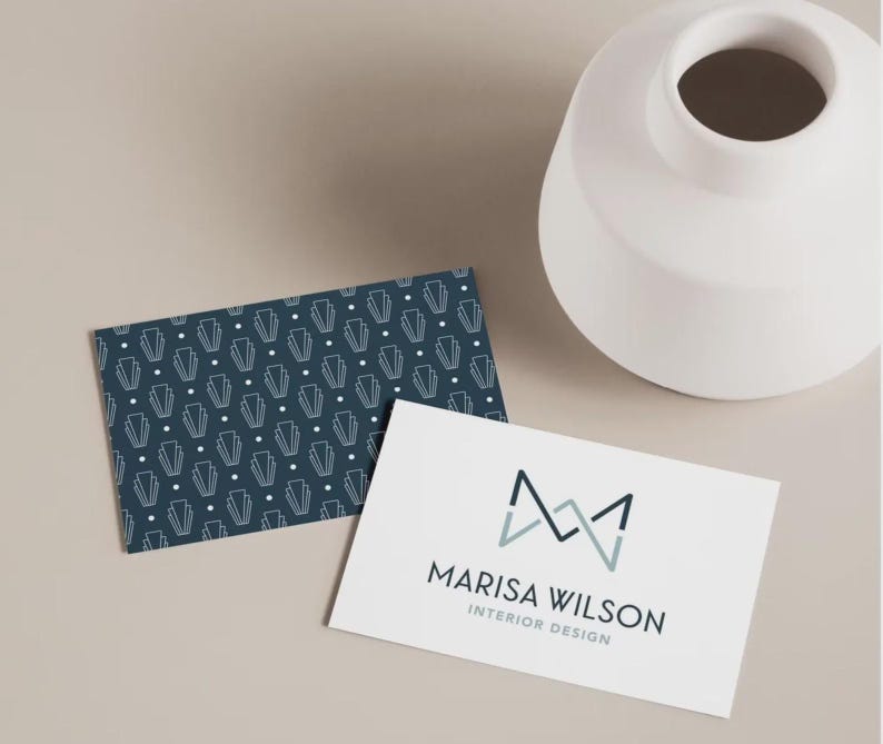May include: Two rectangular business cards. One card features a dark blue background with a repeating white geometric pattern of lines and dots. The other card is white with a dark blue and light blue logo and the text MARISA WILSON INTERIOR DESIGN.