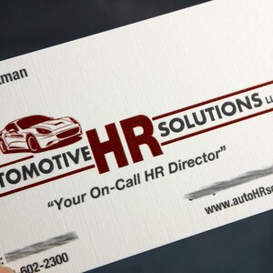 K&ouml;nnte beinhalten: Eine wei&szlig;e Visitenkarte mit einer roten Grafik eines Sportwagens und dem Text Automotive HR SOLUTIONS LLC. Die Karte enth&auml;lt den Schriftzug Your On-Call HR Director, eine Website-Adresse sowie teilweise Kontaktinformationen in roter und schwarzer Tinte.