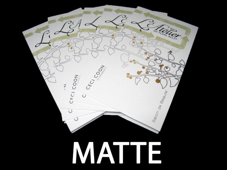 May include: A stack of white rectangular business cards featuring a black line drawing of a leafy branch with gold-colored berries. The text reads L'Atelier de Pearl Alley, Ceci Coon D'Apprenti, and Salon de Beaute, with the word MATTE below.